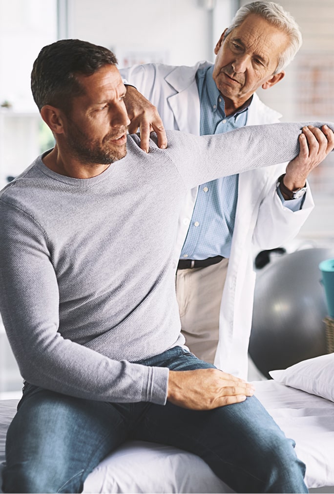 A man in a gray sweater is having his arm examined by a doctor in a white coat. They are in a medical office.