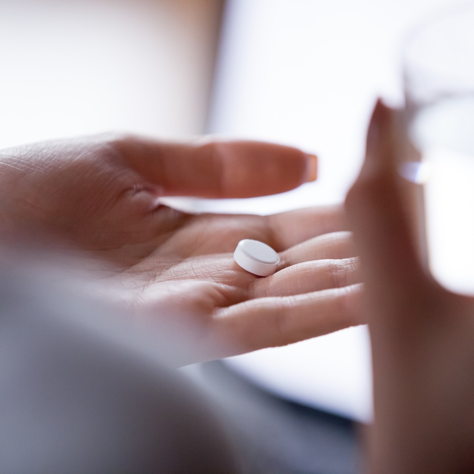 Close up woman holding pill in hand with water. Female going to take tablet from headache, painkiller, medication drinking clear water from glass. Healthcare, medicine, treatment, therapy concept