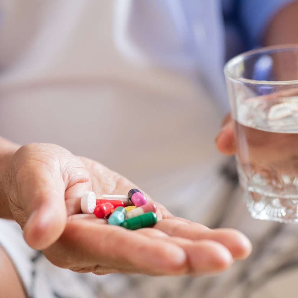 Asian old man taking in pill and another hand holding a glass of clean mineral water. Senior healthcare and medicine concept.