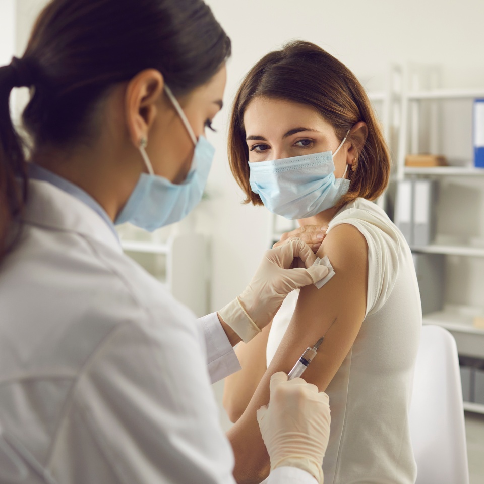 Vaccination, immunization, disease prevention concept. Woman in medical face mask getting Covid-19 or flu vaccine at the hospital. Professional nurse or doctor giving antiviral injection to patient