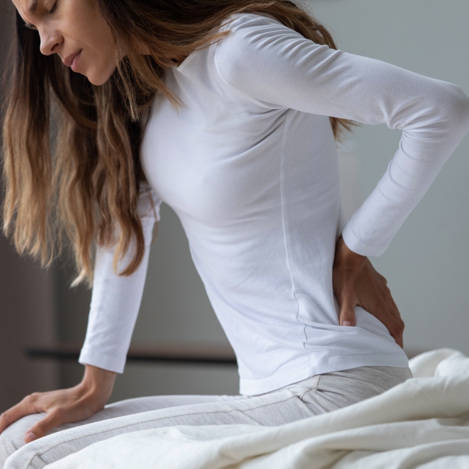 Close up unhappy woman wearing pajama rubbing stiff back muscles after awakening, sitting on bed, upset young female feeling pain, incorrect posture or uncomfortable bed, backache after sleep