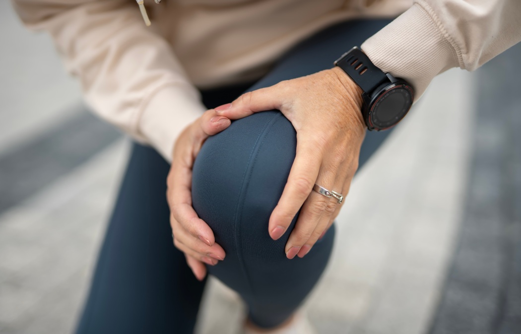 Woman touching her knee in discomfort, experiencing joint pain and injury during or after a physical workout, highlighting common health issues and sports-related problems