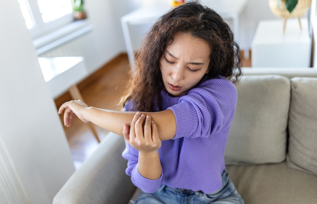 Elbow pain and injury. People with body-muscles problem, Healthcare And Medicine concept. Asian woman sitting on the sofa and holding painful elbow with hand. Joint inflammation and ache concept.